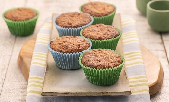 Foto da Receita de Cupcake Leve FiberMais. Observa-se uma tábua de madeira sobre um guardanapo listrado e os cupcakes em cima em forminhas verdes e azuis.